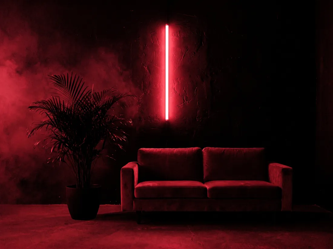 A single velvet sofa alone in a dark room beside one thin line of red neon.